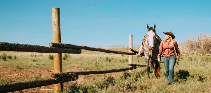 A woman and a horse walking beside a rail fence in a rural U.S. location.