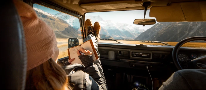 A woman in a Land Rover in New Zealand with her feet on the dashboard looking at mountains.