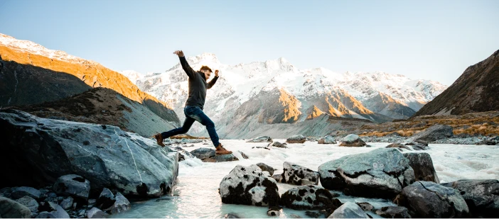 A man jumping from one rock to another in a river in New Zealand.